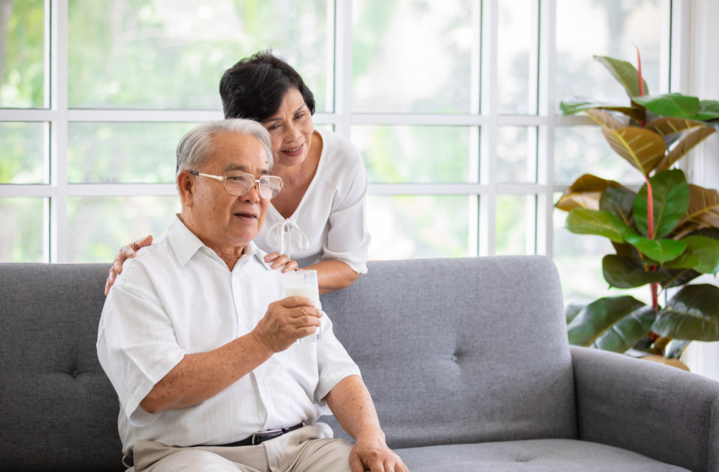 Senior couple hugging one another while sitting and standing close to couch in senior community