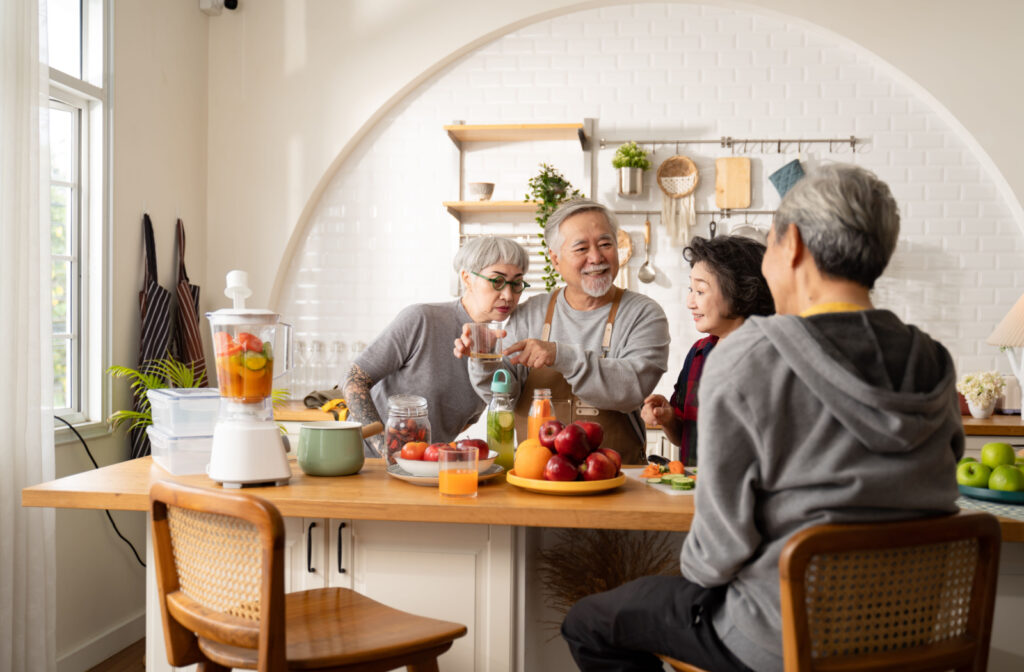 A group of seniors standing around a kitchen island that's filled with fruits, vegetables, and a blender. One woman is smelling fruit juice as a man holds the glass.