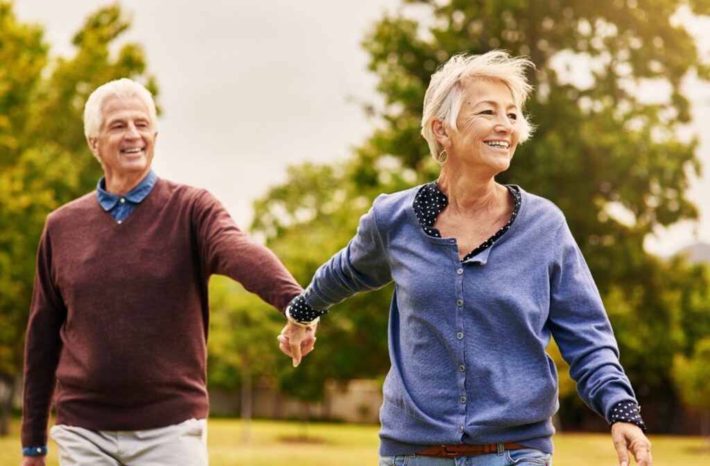 2 older adults holding hands while walking in a park