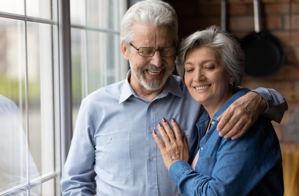 An older couple hugging while looking out the window of their new home in independent living.
