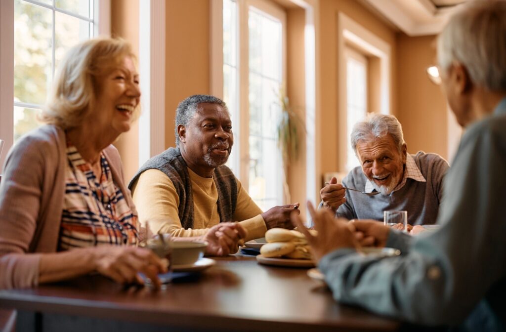 A group of seniors sitting at a dining table enjoying a conversation together while eating and laughing